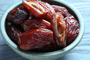 Many tasty dried dates in bowl on blue wooden table, closeup