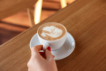 Woman with cup of aromatic coffee at wooden table in cafe, closeup