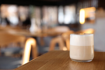 Glass of aromatic coffee on wooden table in cafe, closeup. Space for text