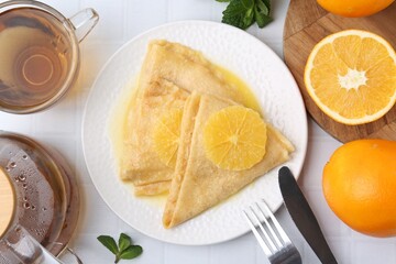 Delicious Crepes Suzette served on white tiled table, flat lay