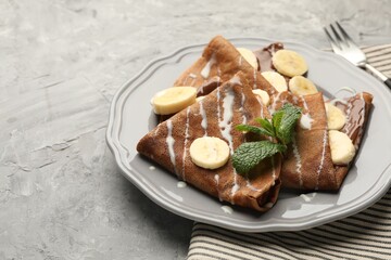 Delicious chocolate crepes with banana, condensed milk and mint served on grey table, closeup
