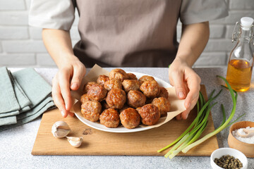 Woman holding plate with delicious meatballs at light textured table, closeup
