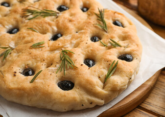Delicious focaccia bread with olives and rosemary on wooden table, closeup
