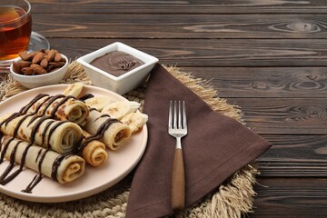 Delicious crepes with chocolate sauce served on wooden table. Space for text