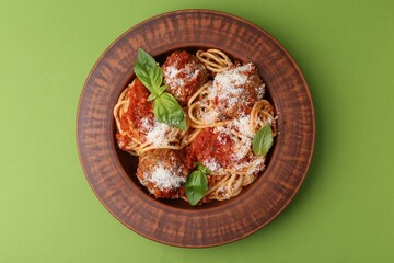 Delicious pasta with meatballs, cheese and basil on green table, top view