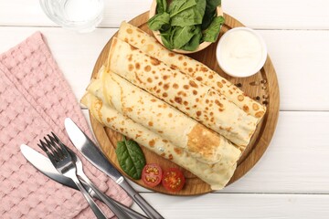 Tasty rolled crepes with cottage cheese and spinach served on white wooden table, flat lay