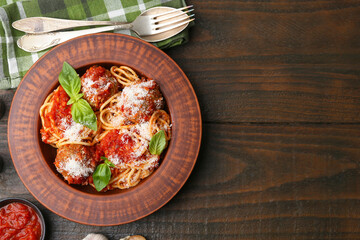 Delicious pasta with meatballs, cheese, basil and tomato sauce on wooden table, flat lay. Space for text