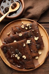 Delicious chocolate crepes with pine cone jam and nuts on wooden table, flat lay