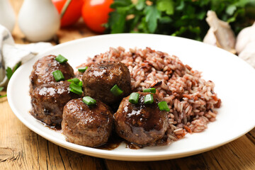 Tasty meatballs with sauce, brown rice and green onion on wooden table, closeup