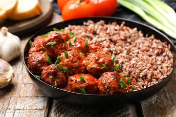 Tasty meatballs with sauce, brown rice and products on wooden table, closeup