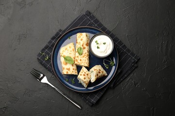 Delicious crepes with cottage cheese, spinach and sour cream served on black table, top view