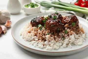Delicious rice with meatballs, sauce and green onions on white table, closeup
