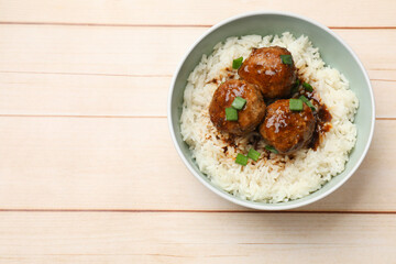 Delicious rice with meatballs, sauce and green onions in bowl on white wooden table, top view. Space for text