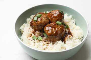 Delicious rice with meatballs, sauce and green onions in bowl on white table, closeup