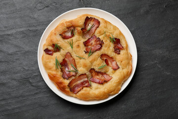 Delicious focaccia bread with bacon and rosemary on black table, top view