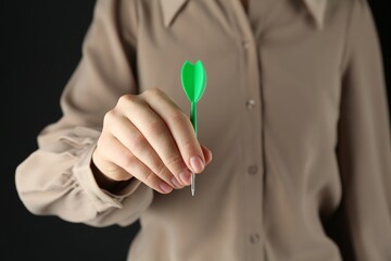 Woman holding dart on black background, closeup
