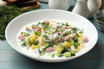Delicious okroshka soup in bowl on light blue wooden table, closeup