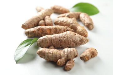 Raw turmeric roots and green leaves on white table, closeup