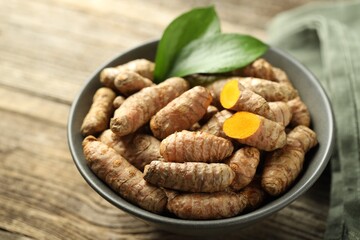 Tumeric rhizomes with leaves in bowl on wooden table, closeup