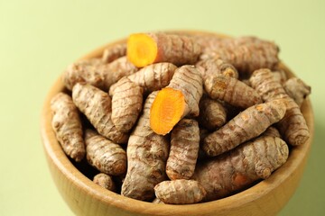 Tumeric rhizomes in bowl on light green background, closeup