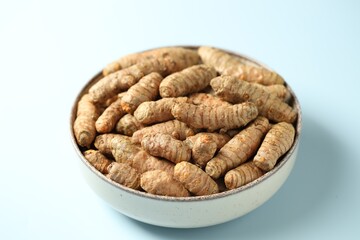 Tumeric rhizomes in bowl on light blue background, closeup