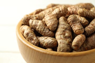 Tumeric rhizomes in bowl on white wooden table, closeup