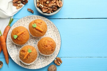 Tasty carrot muffins, walnuts and fresh vegetables on light blue wooden table, flat lay. Space for text