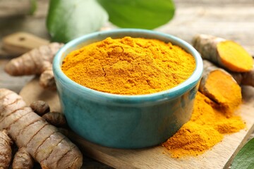 Turmeric powder in bowl and roots on table, closeup
