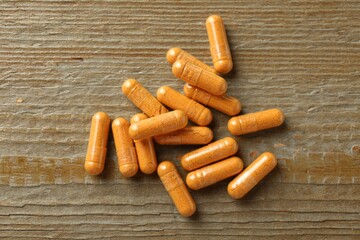Turmeric capsules on wooden table, flat lay