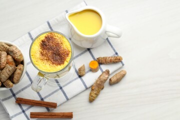 Delicious turmeric latte and rhizomes on white wooden table, flat lay. Space for text