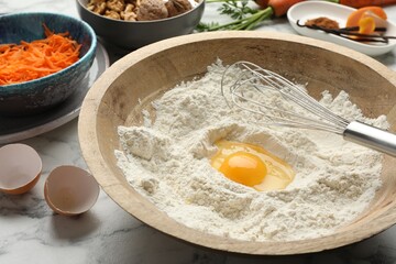 Making carrot cake. Bowl with flour, egg, whisk and other ingredients on white marble table, closeup