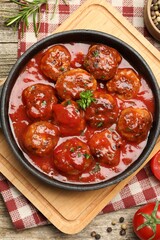 Delicious meatballs with tomato sauce in baking dish on wooden table, flat lay