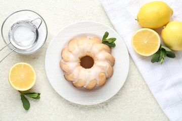 Delicious lemon cake with glaze, mint and citrus fruits on light textured table, flat lay