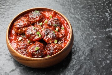 Delicious meatballs with tomato sauce and herbs on black table, closeup. Space for text