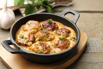 Delicious meatballs with gravy cream sauce and herbs on wooden table, closeup