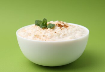 Tasty rice pudding with cinnamon and mint in bowl on green background, closeup