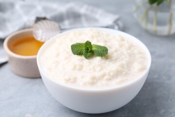 Tasty rice pudding with mint and honey on light grey table, closeup