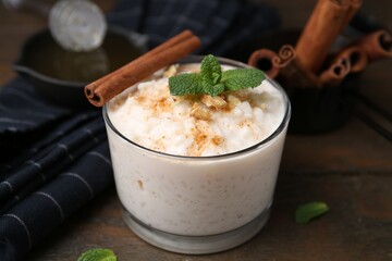 Tasty rice pudding with cinnamon, mint and nuts on wooden table, closeup