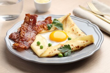 Delicious crepe with egg, bacon and green peas served on wooden table, closeup. Breton galette