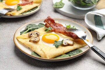 Delicious crepes with eggs, bacon and mushrooms served on grey table, closeup. Breton galette