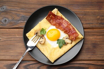 Delicious crepe with egg, bacon and mushrooms served on wooden table, top view. Breton galette
