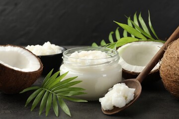 Organic coconut cooking oil in jar, spoon, fresh fruits and green branches on grey table, closeup