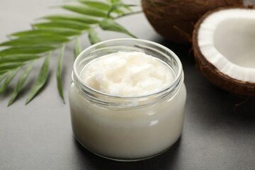 Organic coconut cooking oil in jar, fresh fruits and green branch on grey table, closeup