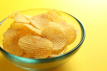 Tasty potato chips on yellow background, closeup