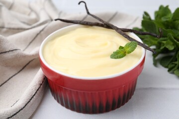 Tasty vanilla pudding, mint and pods on white tiled table, closeup