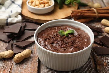 Tasty chocolate pudding in bowl and ingredients on wooden table, closeup