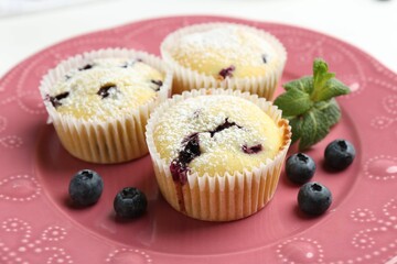 Delicious muffins with blueberries, powdered sugar and mint on white table, closeup
