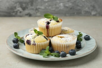 Delicious muffins with blueberries, powdered sugar and mint on grey textured table, closeup