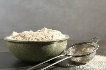 Brown rice flour and sieve on grey table, closeup. Space for text
