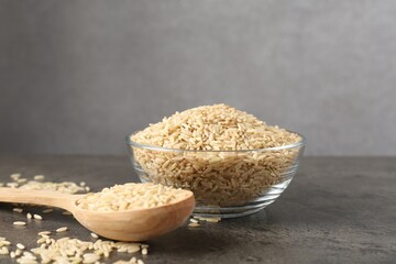 Brown rice in bowl and spoon on grey table. Space for text